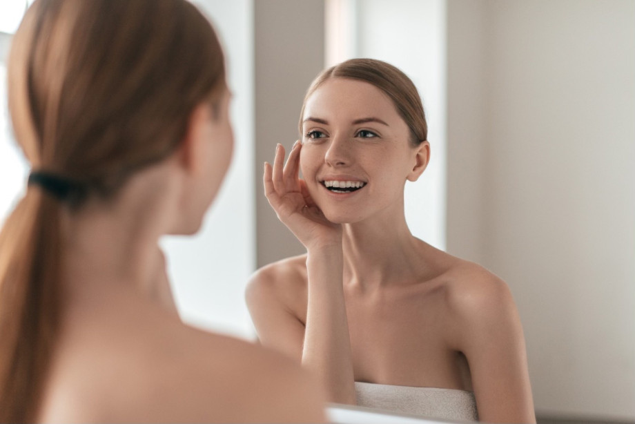 Ce rol are vitamina E în protecția celulară a pielii (femeie fericita care se uita in oglinda, skincare, baie)